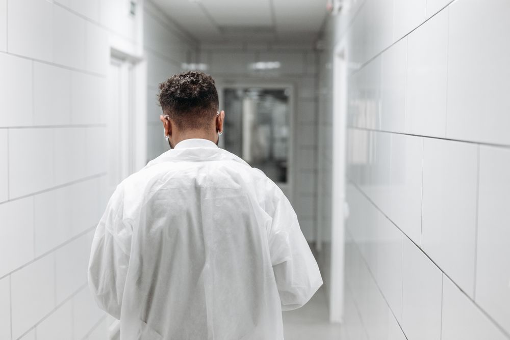 A clinician in a lab coat walking along a bright hospital corridor.