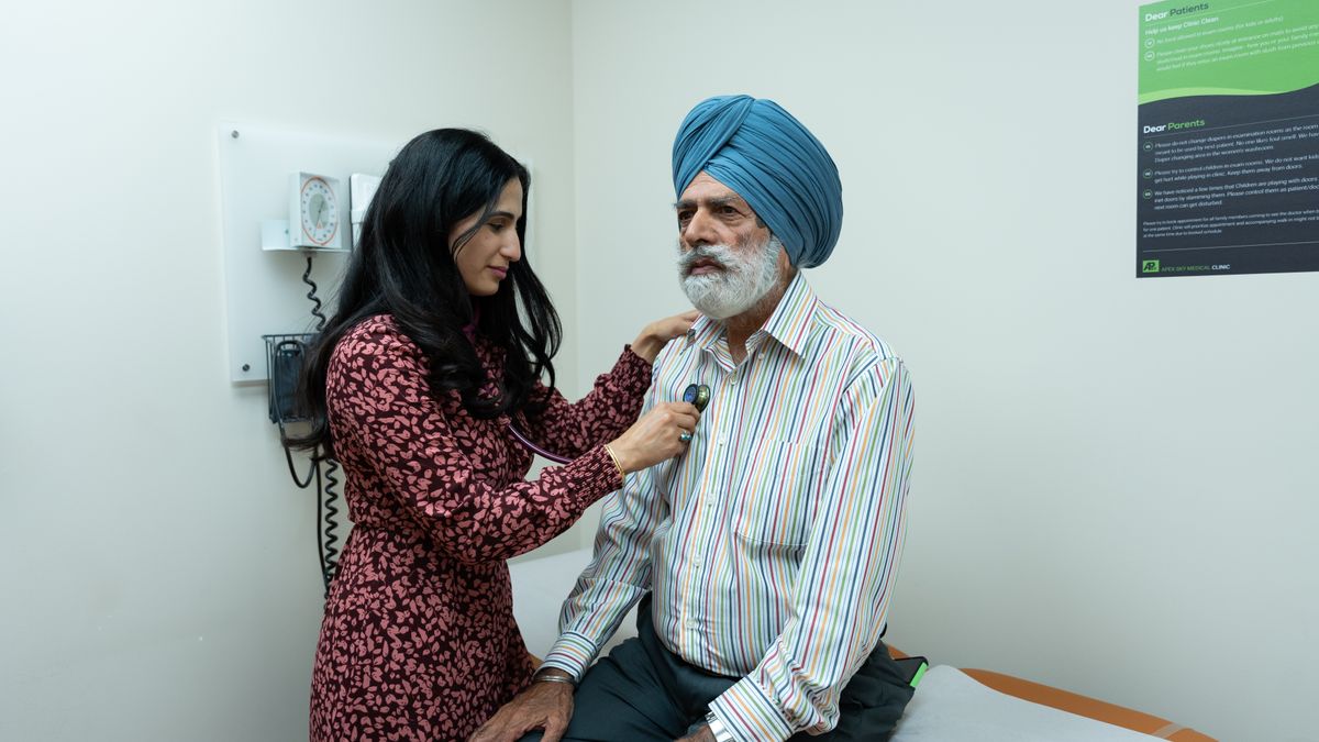 A clinician assisting an elderly patient in a consulting room.